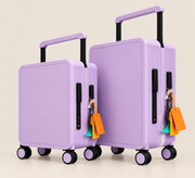Two lavender purple hard-shell spinner suitcases with telescoping handles and colorful shopping tags, shown on a clean light beige studio background.